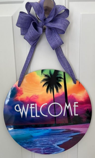 Round welcome sign featuring a colorful sunset, palm trees, and a beach scene.