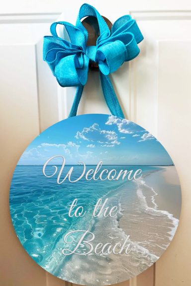 Round sign with blue ocean and sand, featuring "Welcome to the Beach" text.