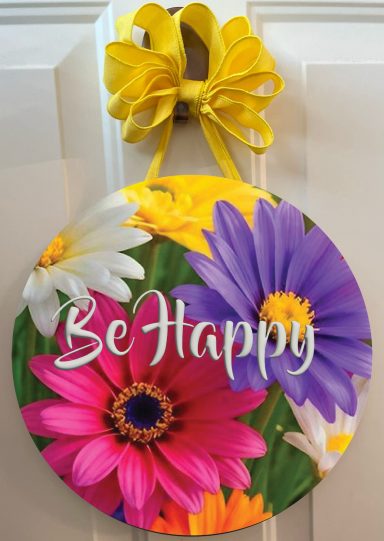 Round wall decor featuring colorful flowers and the phrase "Be Happy."