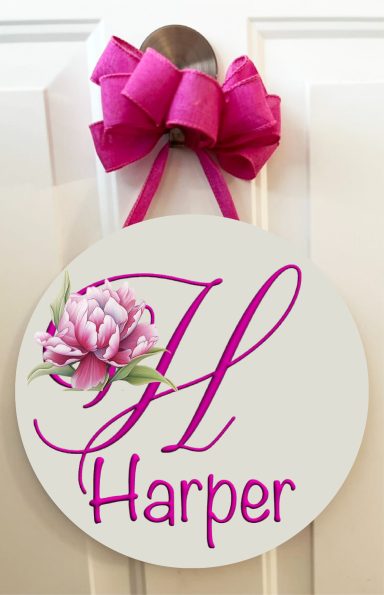 Circular door sign with the name "Harper" in pink and a floral design, topped with a pink bow.