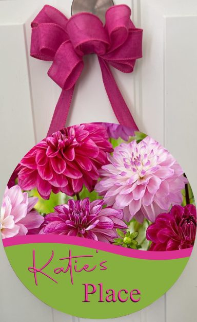 Circular sign featuring colorful flowers and the text "Katie's Place" with a pink ribbon.
