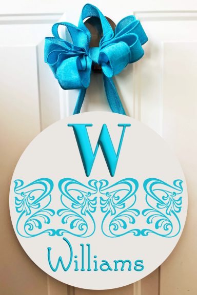 Round sign with a blue "W" and ornate lace design, reading "Williams," decorated with a bow.