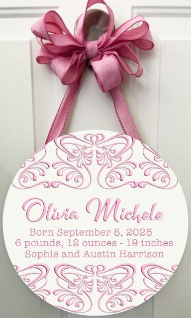 Round pink birth announcement with details about baby girl, adorned with a pink ribbon.