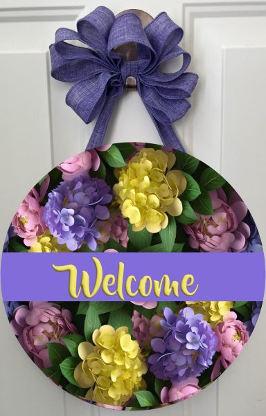 Circular welcome sign adorned with colorful flowers and a purple bow.